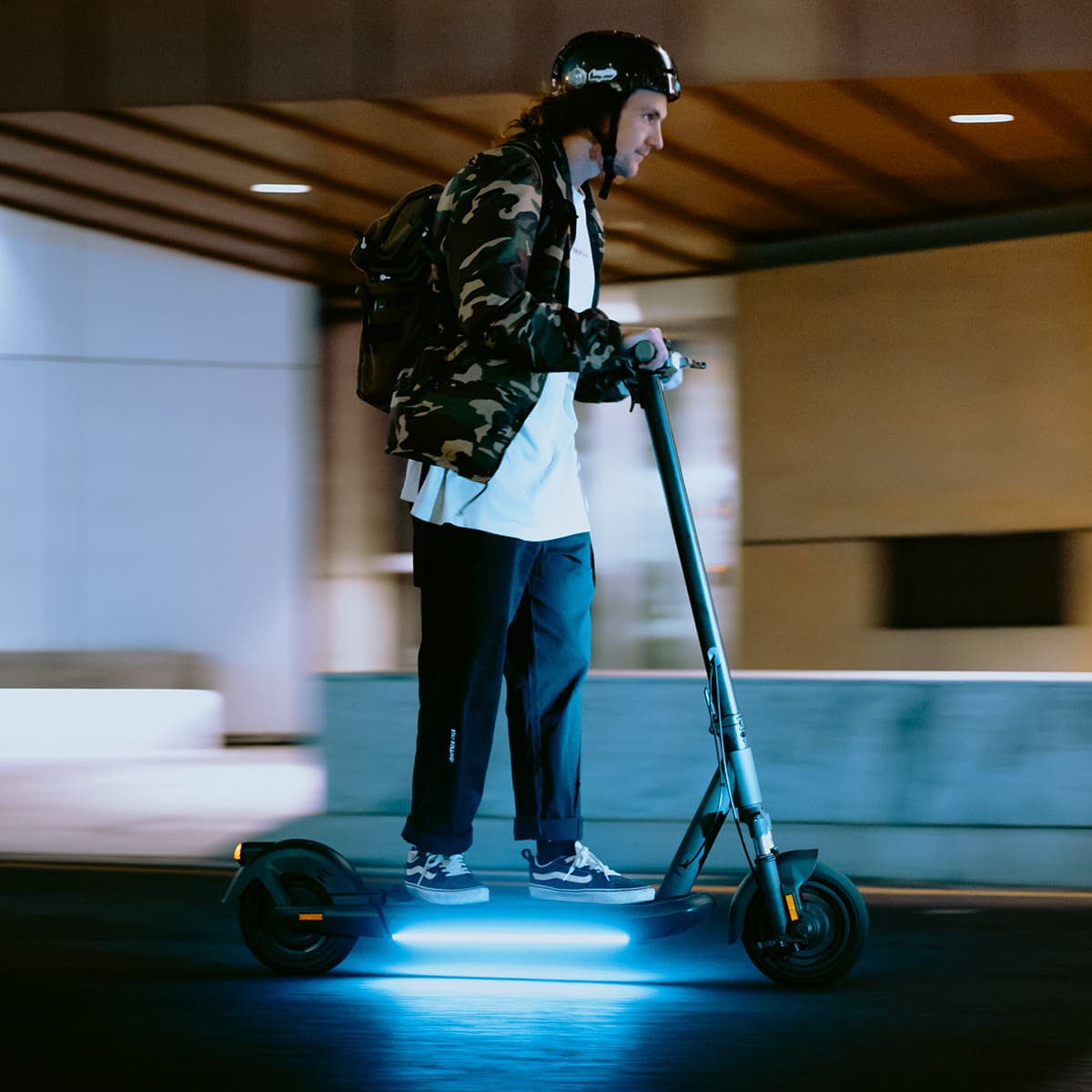 Rider on INMOTION S1F electric scooter with blue lights in urban night setting.