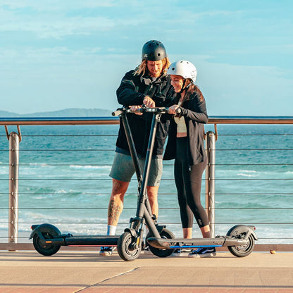 Couple reviewing INMOTION S1F scooters by the ocean on a sunny day