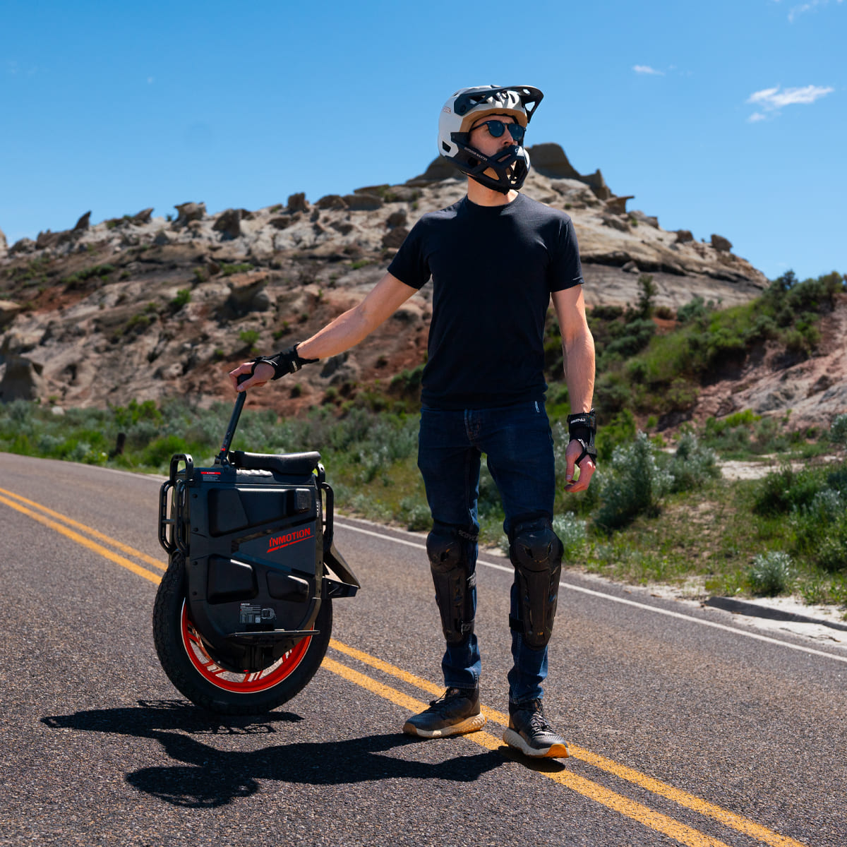 Rider holding INMOTION V13 Pro unicycle on a road with mountains in the background.