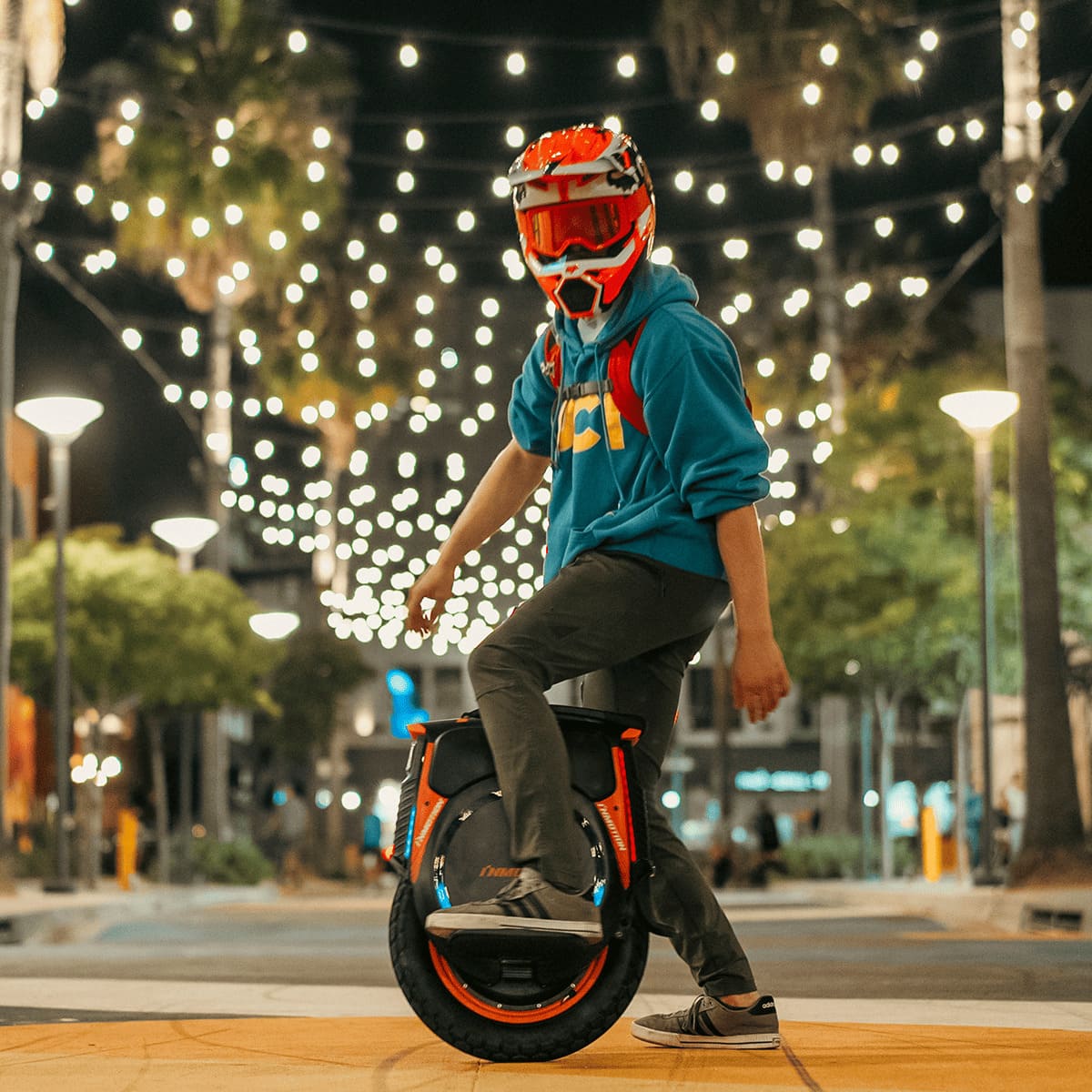 Rider in helmet showcasing INMOTION V12 Pro unicycle under string lights at night.