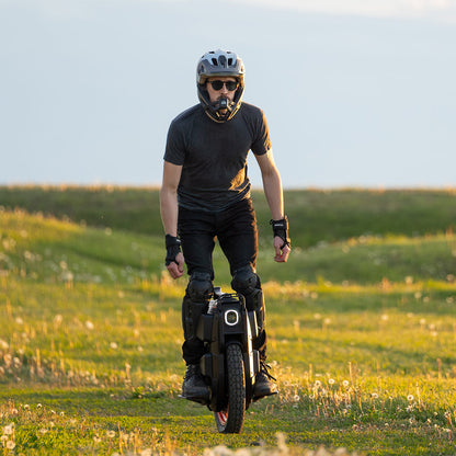 Rider balancing on INMOTION V13 Pro unicycle in grassy field.